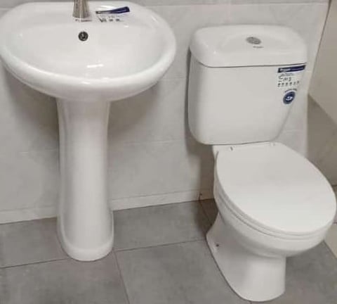 Modern white bathroom fixtures including a pedestal sink on the left and a toilet with cistern on the right against tiled walls