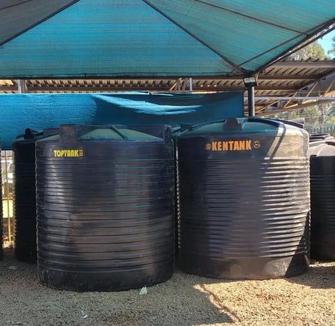 Two black cylindrical water storage tanks labeled Kentank under a blue shade structure, with corrugated metal roof visible in background