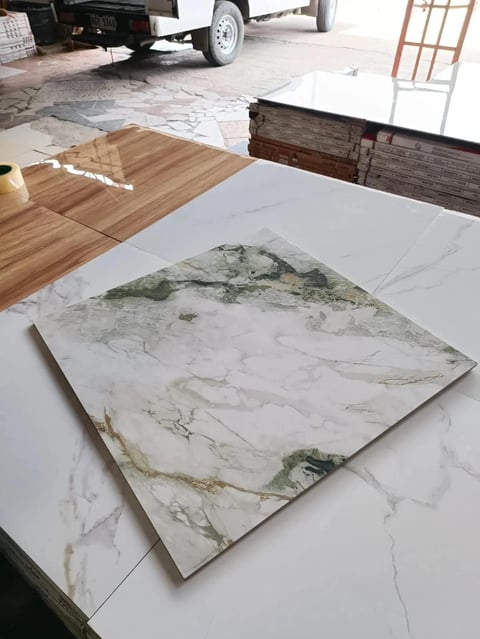 Marble tile samples displayed on white surface with wood flooring and truck in background at outdoor showroom