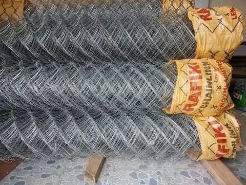 Rolls of galvanized chain-link fencing mesh stacked horizontally with packaging labels visible