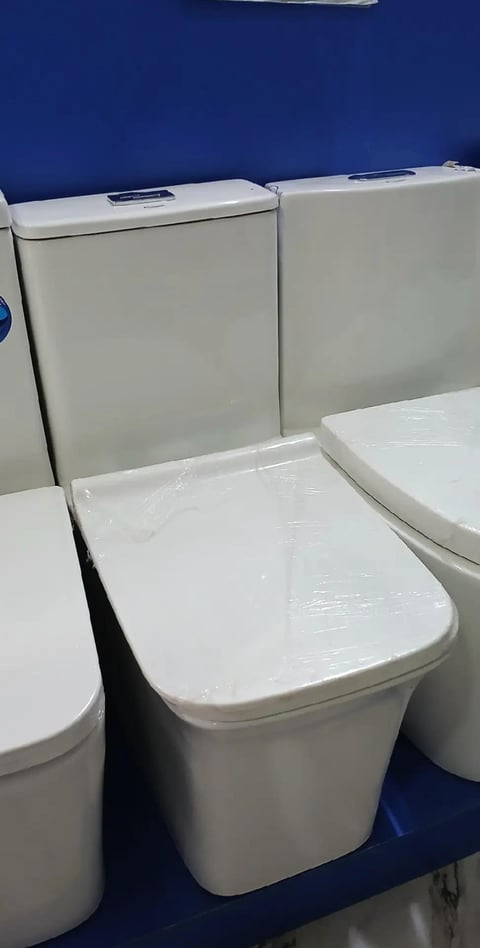 White modern toilet models displayed in a showroom with blue wall background and open lids showing tanks