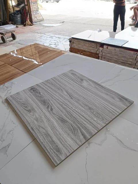 Flooring showroom displaying various tile and wood samples on white surface, with stacked materials in background