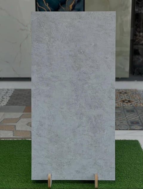 Light gray concrete tile sample displayed vertically on green surface in showroom with other flooring samples in background