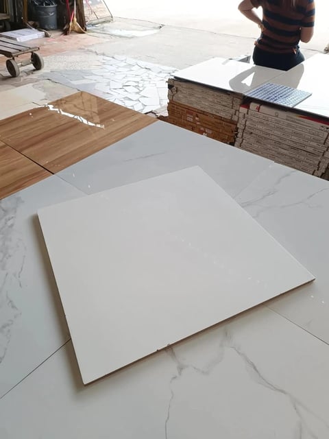 Marble-look tile samples and wood flooring samples displayed on a construction floor with blueprints and materials in background