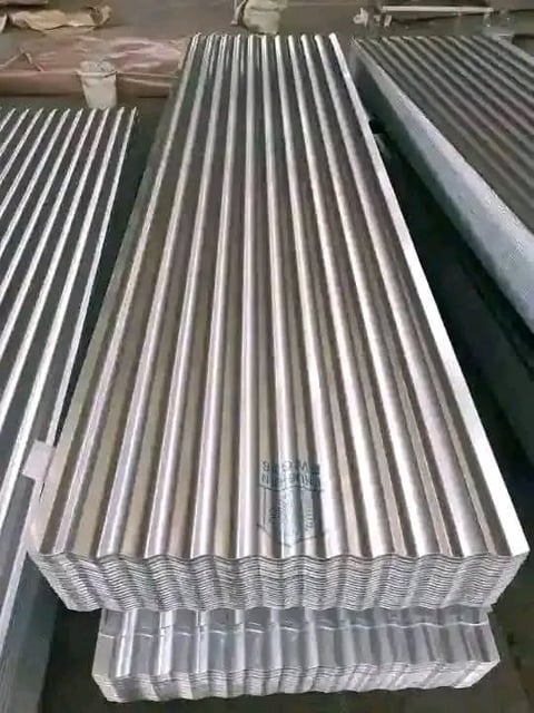 Stack of corrugated metal sheets with parallel ridges and grooves in an industrial warehouse setting