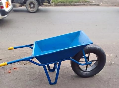 Blue wheelbarrow with single black wheel parked on paved ground near vehicles