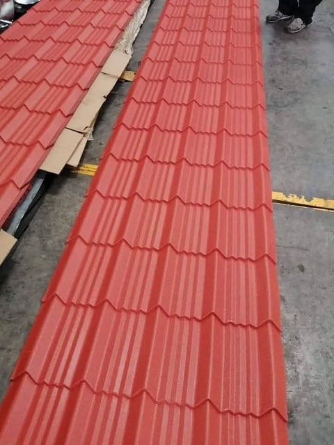 Red corrugated metal roofing tiles arranged on ground at construction site with measurement tape