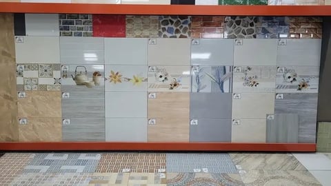 Tile and flooring showroom display featuring various ceramic and stone samples arranged on a wall grid with decorative borders.