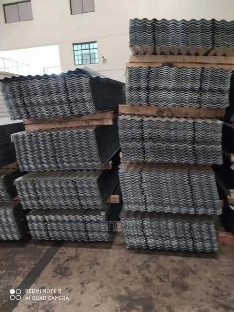 Stacked bundles of gray wavy roof tiles organized in two piles inside an industrial building with white walls and small windows