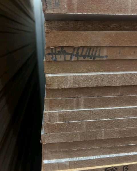 Close-up of stacked wooden planks with graffiti marking and white paint lines, with black object on left edge