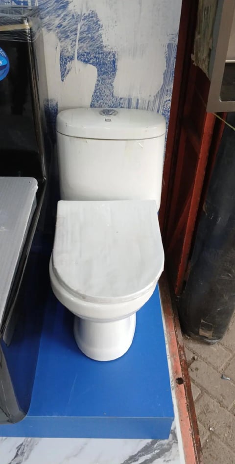White ceramic two-piece toilet with seat open, displayed on a blue platform in a showroom