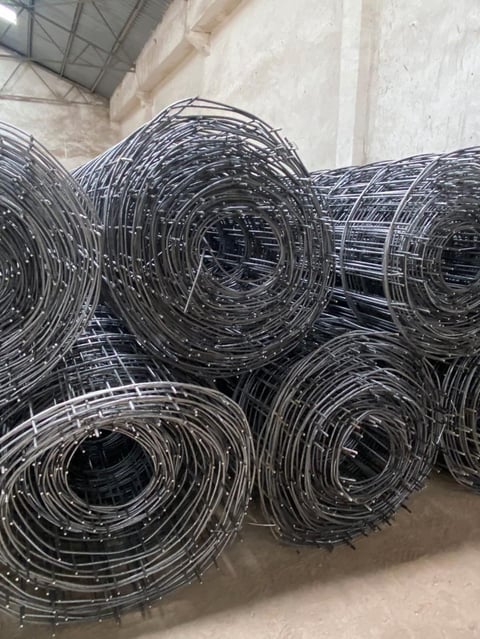 Rolls of black wire mesh fencing stored in an industrial warehouse setting