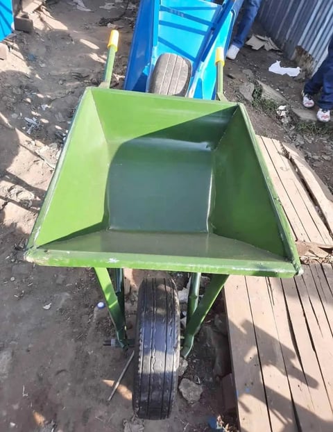 Green wheelbarrow with open bin body and black pneumatic tire, photographed from above in outdoor storage area