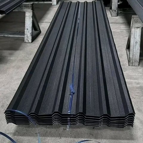 Stack of black metal corrugated roofing sheets on concrete floor in warehouse