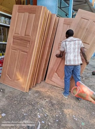 Man examining stacked wooden doors and panels at a construction supply yard