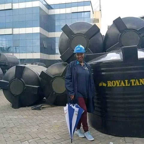 Worker in hard hat and company uniform standing in front of large black industrial storage tanks with office building in background