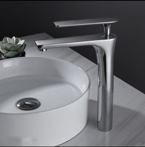 Modern bathroom sink setup with white round vessel sink, chrome waterfall faucet, and small succulent plant on gray counter