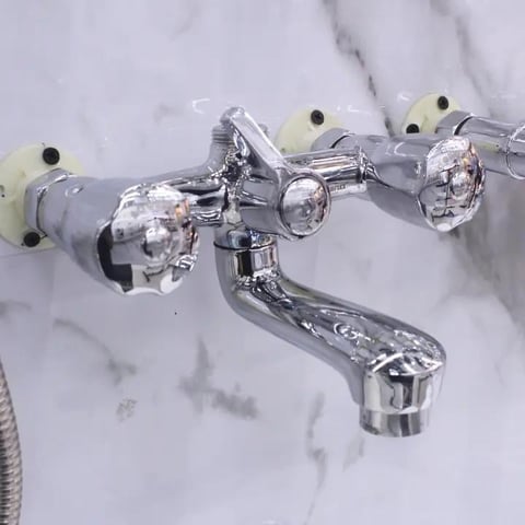 Chrome wall-mounted bathroom faucet with two crystal knobs and spout on marble wall