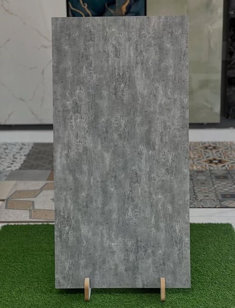 A rectangular gray concrete tile sample displayed on artificial green grass with wooden supports in a showroom setting.