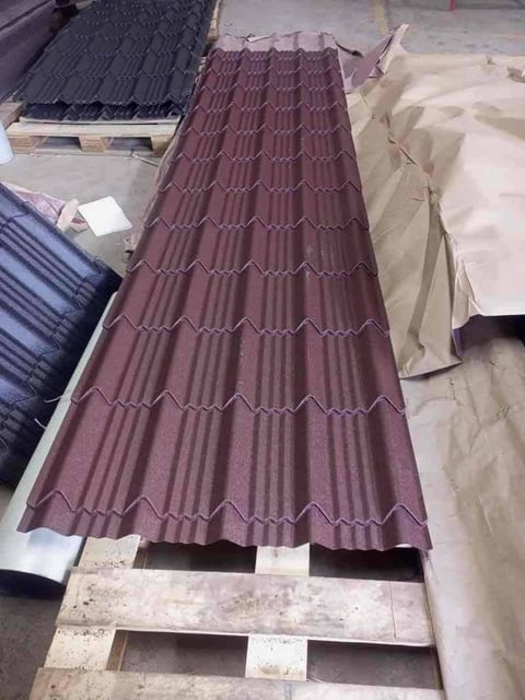 Burgundy corrugated metal roofing panels stacked on wooden pallets in a warehouse or construction storage area