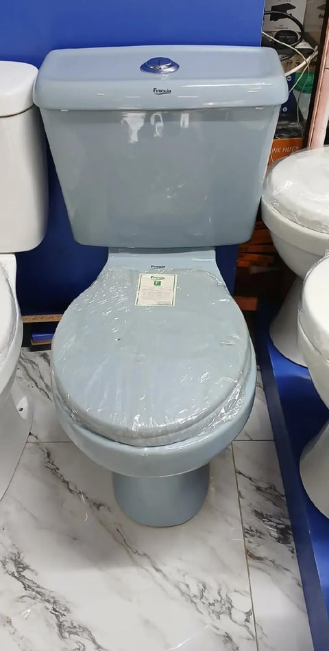 Light blue ceramic toilet with matching tank on marble-effect floor in showroom display, shrink-wrapped seat visible